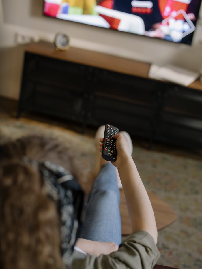 our-story A woman relaxes on a couch inside her cozy home, watching television with a remote in hand.